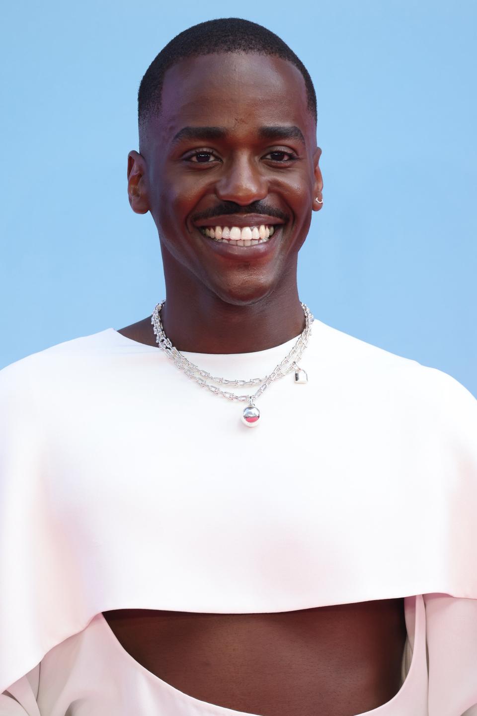 Ncuti in stylish white top with cutouts and sparkling necklace smiles at event