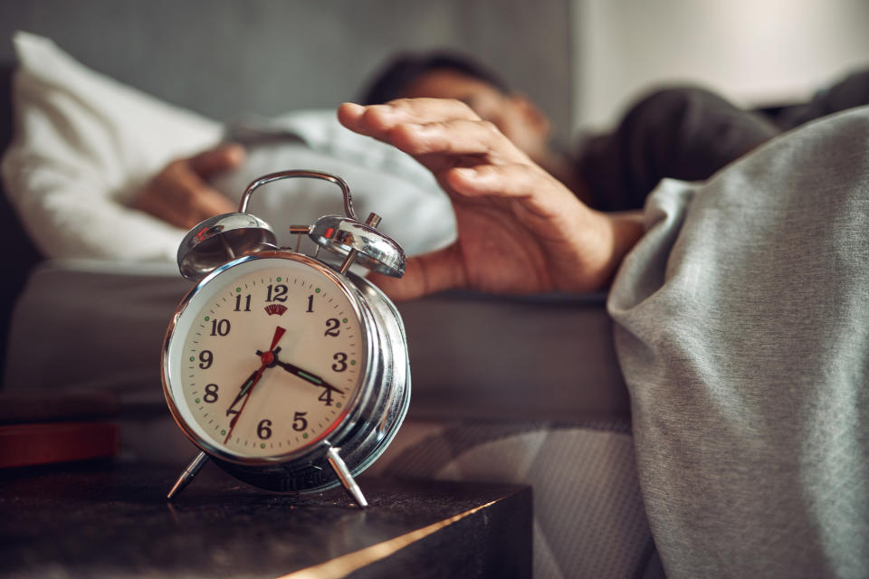 someone reaching for the clock while in bed