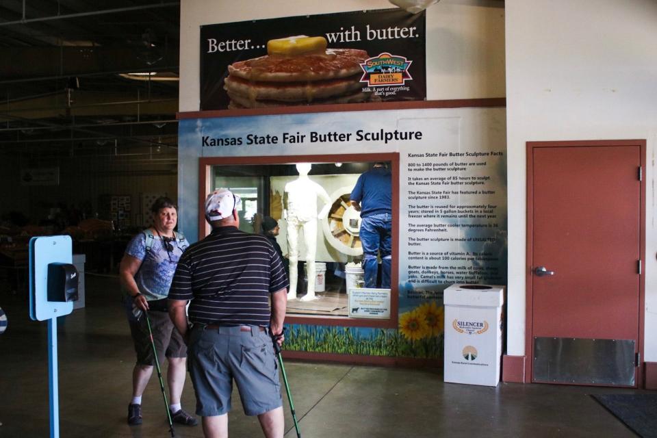 A man reads facts about the Kansas State Fair butter sculpture early Friday morning. A sign reading "Better ... with butter" is pinned above the glass.