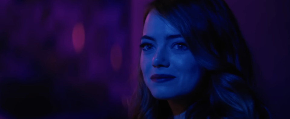 A woman in blue lighting smiles at someone off screen