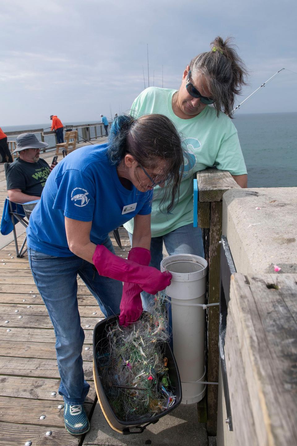 Jen Starr disposes of paper, plastic, and organic material tangled up in fishing lines and discarded tackle collected on Navarre pier while Amber Bennett looks on, on Thursday, April 18, 2024. The Navarre transplant has been collecting and recycling monofilament fishing line and tackle at the pier for the last two years.