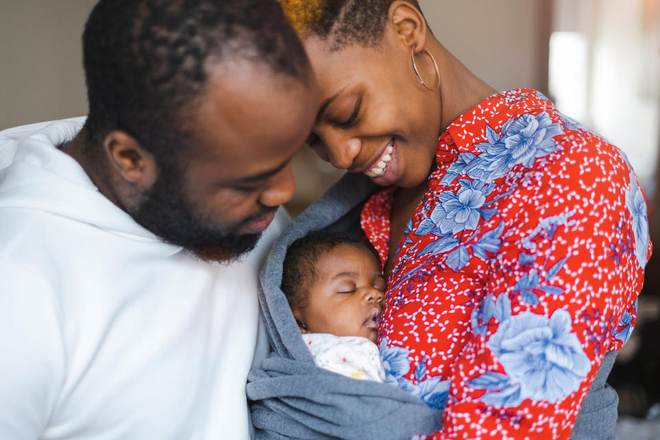 Man and woman smile affectionately while holding a sleeping baby wrapped in a blanket