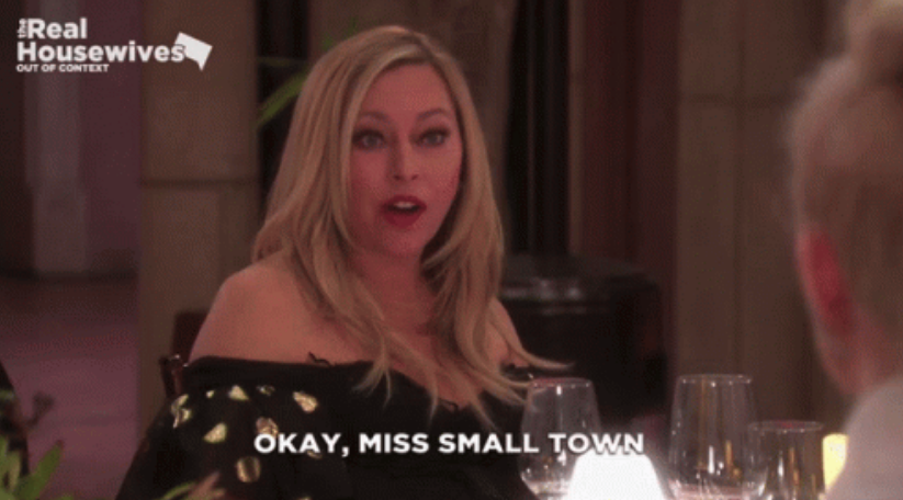 Sutton Stracke from The Real Housewives of Beverly Hills talking at a dinner table with the text overlay "OKAY, MISS SMALL TOWN."