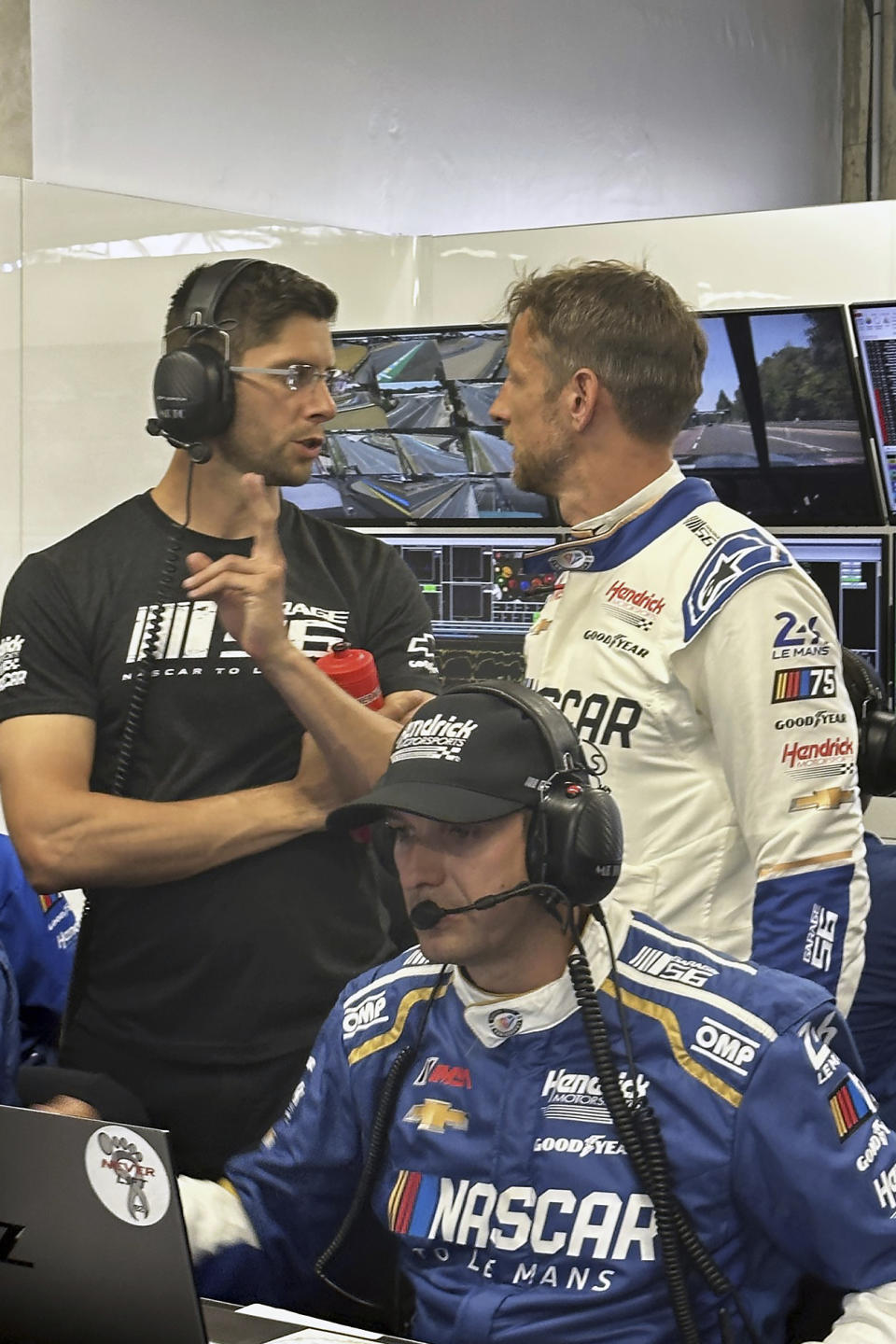 Sports car driver Jordan Taylor, left, talks with 2009 Formula One champion Jenson Button during practice for the 24 Hours of Le Mans auto race in Le Mans, France, Thursday, June 8, 2023. Hendrick project manager Greg Ives is in the foreground. Taylor helped develop the Garage 56 car that will be driven by Button, Jimmie Johnson and Mike Rockenfeller. (AP Photo/Jenna Fryer)