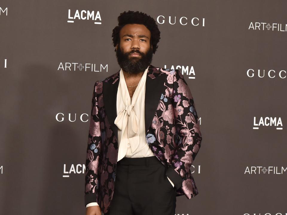 Donald Glover at an event in 2019. He wears a blazer with purple flowers over a white shirt.