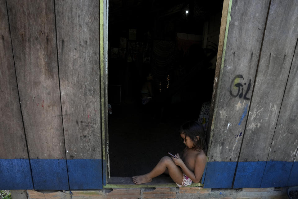 A Tembe girl plays with a smartphone at the door of her house in the Tenetehar Wa Tembe village in the Alto Rio Guama Indigenous territory, in Paragominas municipality, in Para state, Brazil, Friday, June 9, 2023. (AP Photo/Eraldo Peres)