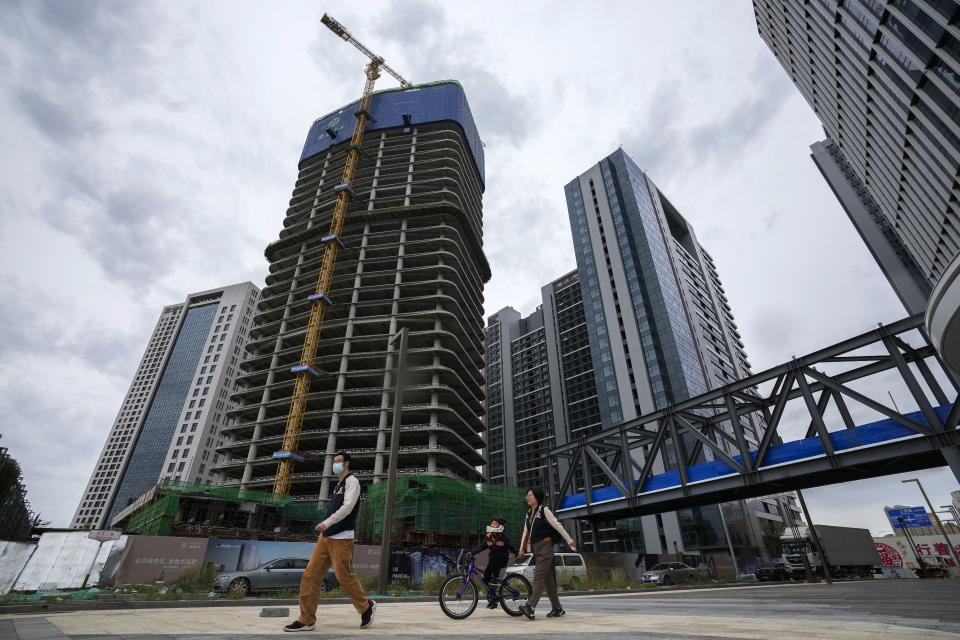 A family walks by a commercial office buildings under construction in Tongzhou, outskirts of Beijing, Monday, Oct. 4, 2021. China’s economy is losing steam as President Xi Jinping's government cracks down on corporate debt and energy use in pursuit of more stable, sustainable growth. (AP Photo/Andy Wong)