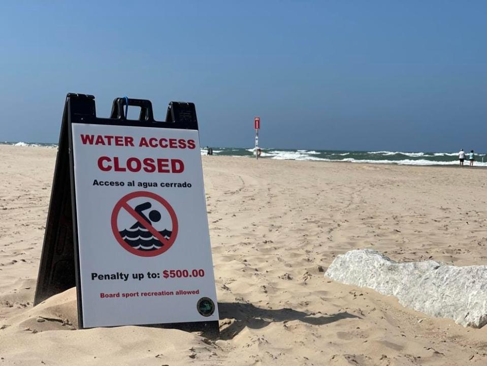 A sign warns of penalties for entering the water while double red flags are flying in Grand Haven.