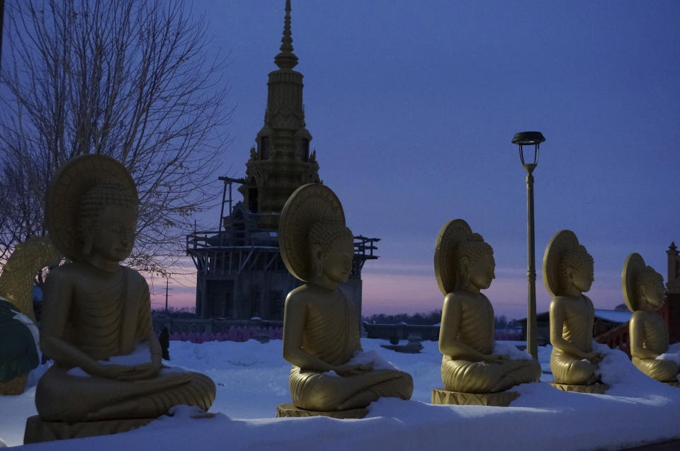 Estatuas de Buda y la estupa que alberga sus reliquias al anochecer en el complejo del templo Watt Munisotaram el sábado 4 de febrero de 2023 en Hampton, Minnesota. (AP Foto/Giovanna Dell'Orto)