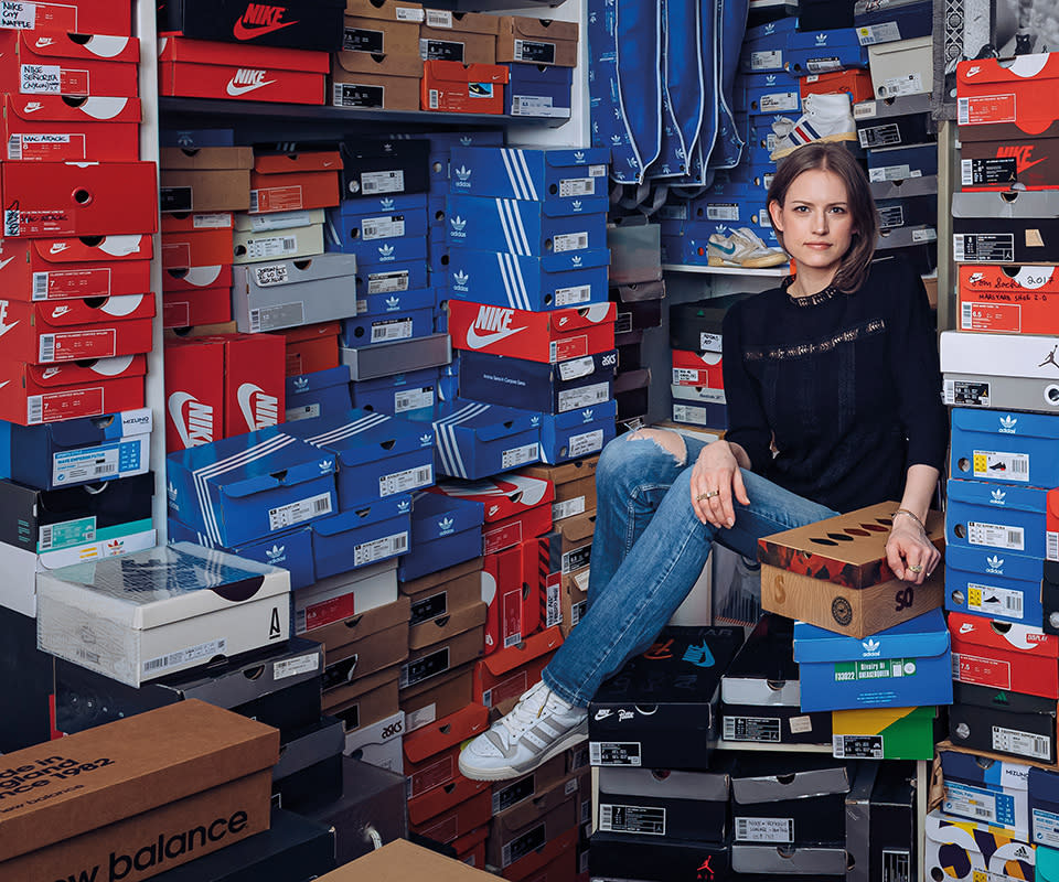 Julia Schoierer, aka sneakerqueen, sits among stacks of sneakers piled high on shelves and on the ground all around her.
