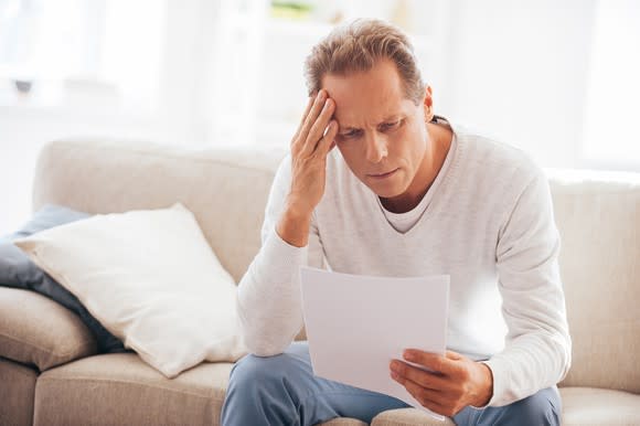 Man holding his head with concerned expression while reading a document