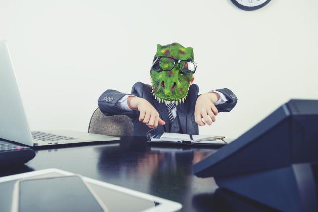 young boy dressed in a suit working at a large desk he is wearing a monster dinosaur mask