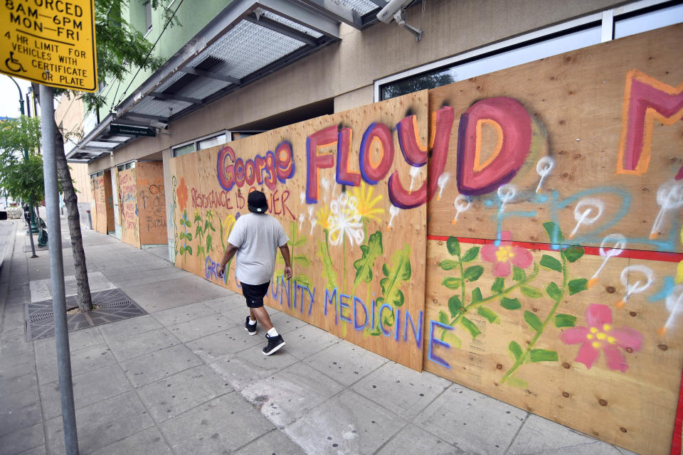 A pedestrian passes a colorful painted tribute to George Floyd on a boarded-up business, Thursday, June 18, 2020 in Minneapolis. Scores of businesses along Lake Street remain boarded up following riots, fires and looting. Floyd died in police custody after video shared online by a bystander showed former officer Derek Chauvin kneeling on Floyds' neck during his arrest as he pleaded that he couldn't breathe. (AP Photo/Jim Mone)