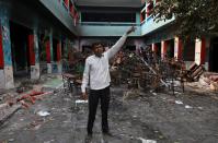 A man points towards a damaged portion of a school building that was attacked by a mob in a riot affected area following clashes between people demonstrating for and against a new citizenship law in New Delhi