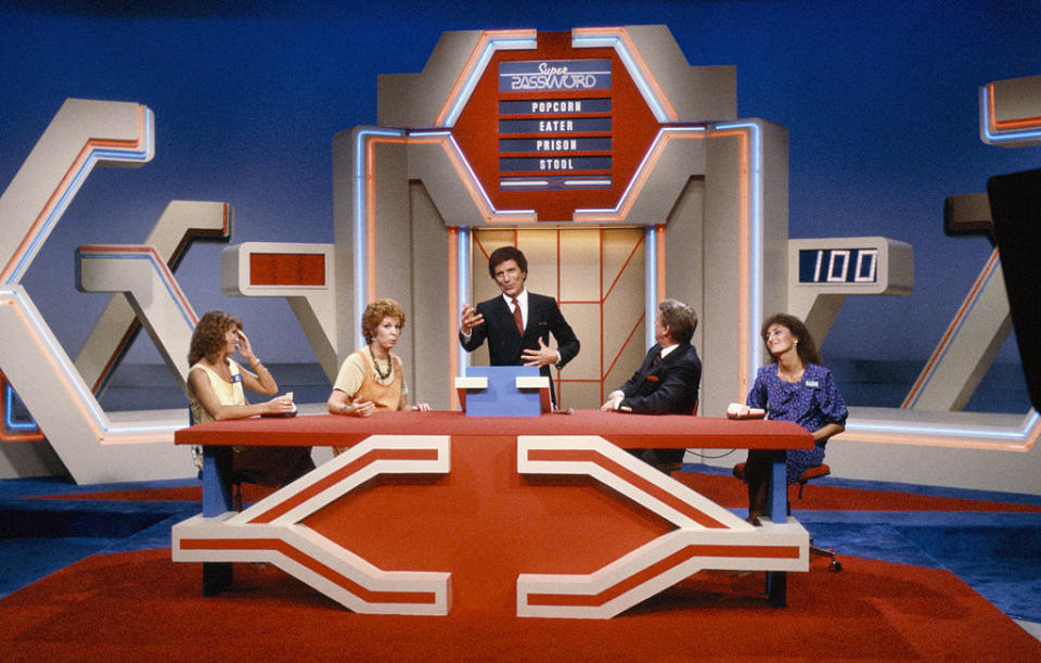 Four contestants and a host on the set of the game show "Super Password."