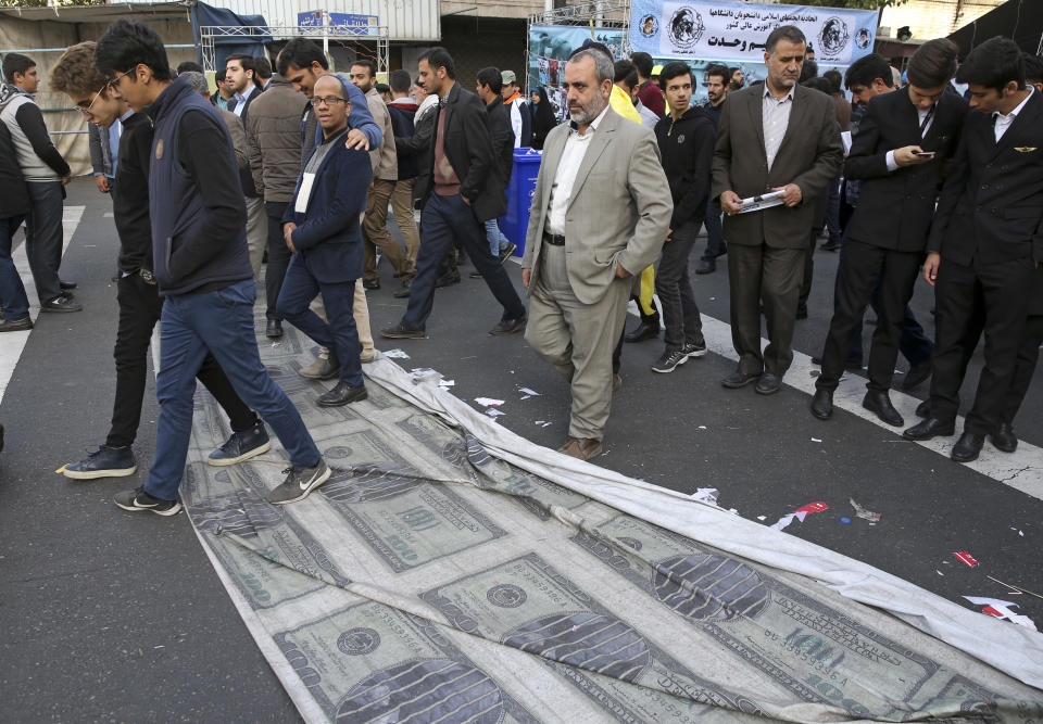 Demonstrators walk on a banner showing altered images of U.S. banknotes with a picture of President Donald Trump on the ground during a rally in front of the former U.S. Embassy in Tehran, Iran, on Sunday, Nov. 4, 2018, marking the 39th anniversary of the seizure of the embassy by militant Iranian students. Thousands of Iranians rallied in Tehran on Sunday to mark the anniversary as Washington restored all sanctions lifted under the nuclear deal. (AP Photo/Vahid Salemi)