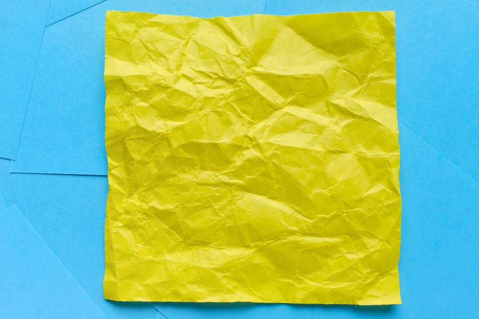 A crumpled yellow paper square lies on a flat blue background