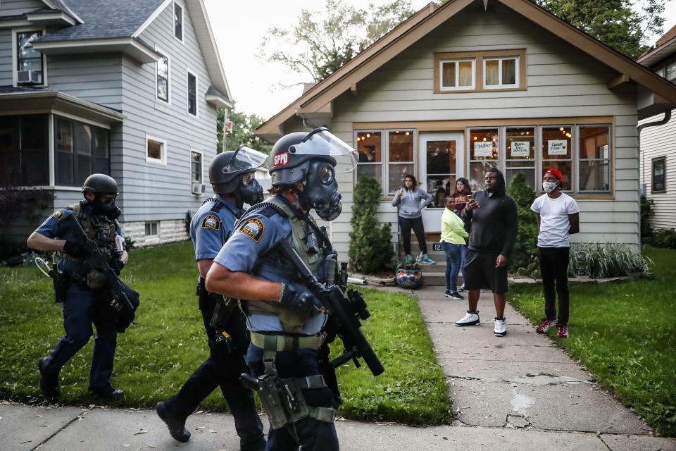 FILE - In this May 28, 2020, file photo, protesters and residents watch as police in riot gear walk down a residential street, in St. Paul, Minn. Reports of hateful and violent speech on Facebook poured in on the night of May 28 after President Donald Trump hit send on a social media post warning that looters who joined protests following Floyd's death last year would be shot, according to internal Facebook documents shared with The Associated Press. (AP Photo/John Minchillo, File)