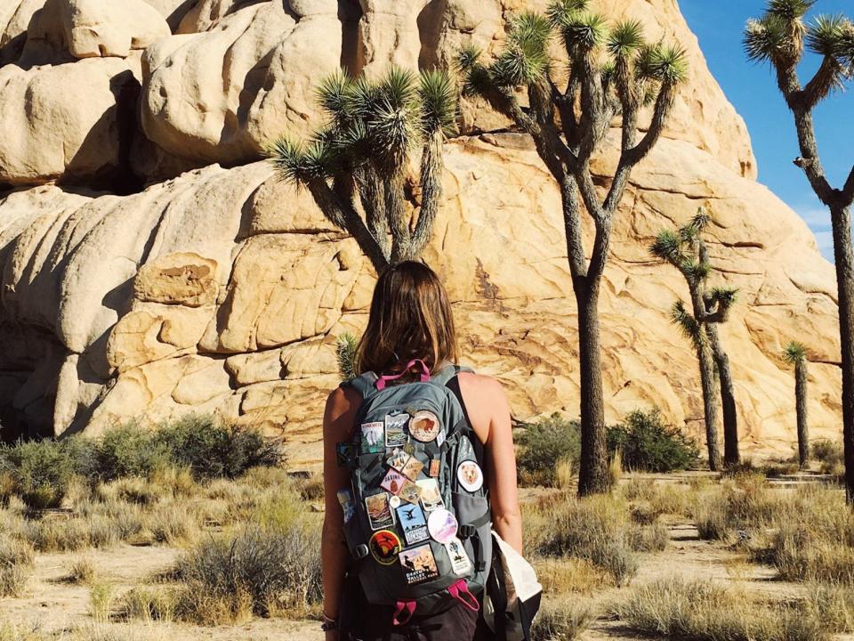 Emily facing a rock formation that is surrounded by Joshua trees at Joshua Tree National Park.