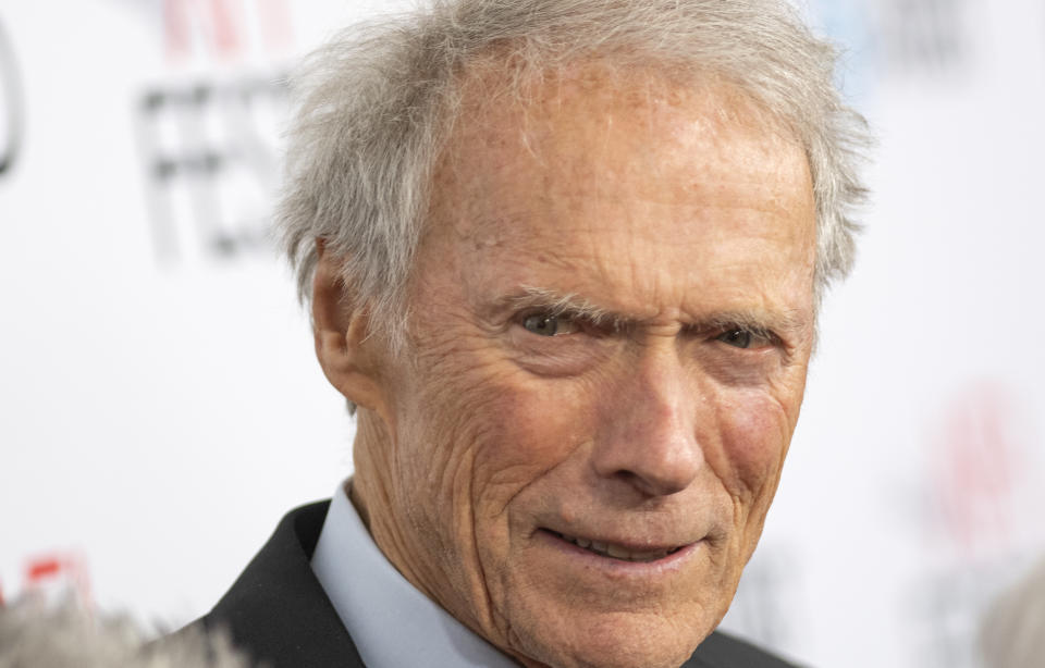 Clint Eastwood at an event, wearing a suit and tie, on a red carpet backdrop