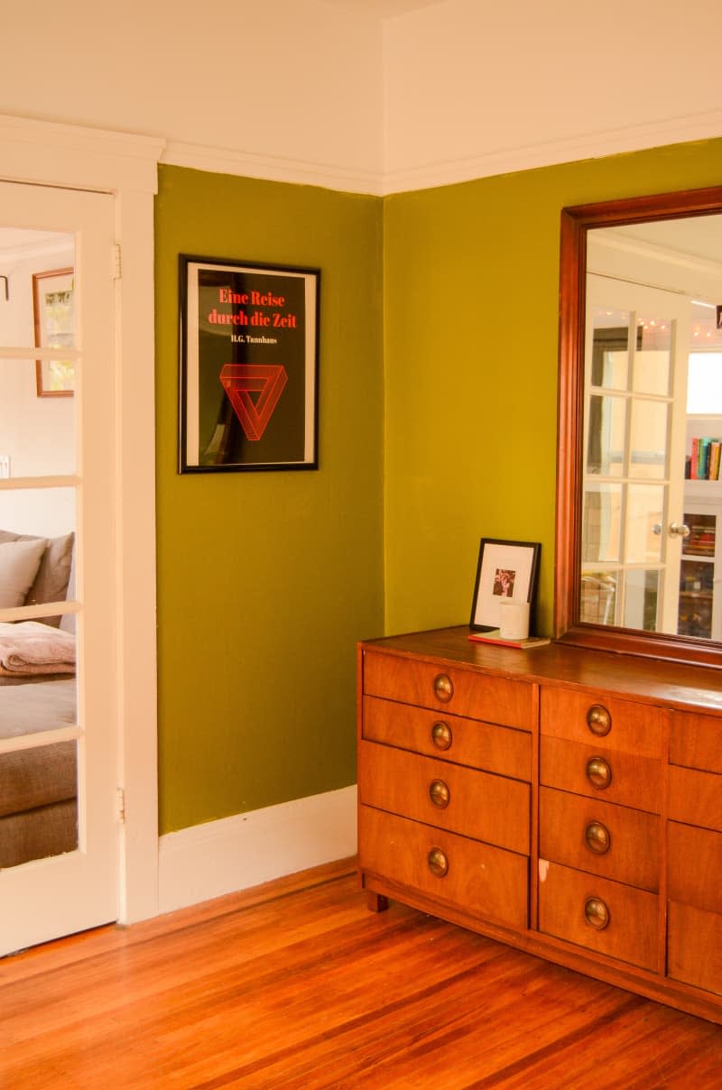 Green walled bedroom with framed art and mirrored dresser.