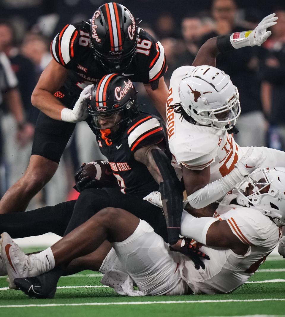 Texas linebacker Jaylan Ford, bottom, brings down Oklahoma State running back Ollie Gordon II (0) with help from Texas defensive back Jahdae Barron in Texas' 49-21 win in the Big 12 title game Saturday game at AT&T Stadium in Arlington. Gordon, the top rusher in FBS, had just 34 yards on the ground against Texas.