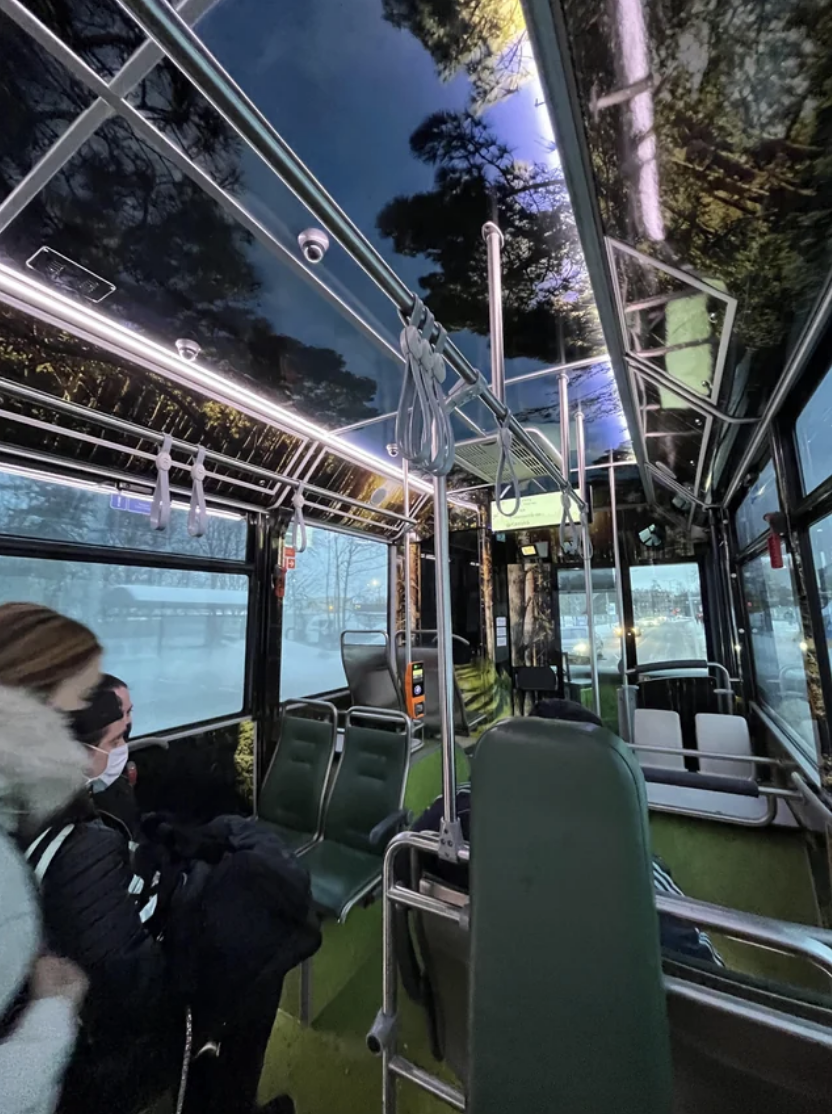 Interior of a bus with passengers seated and standing handholds evident, nighttime outside