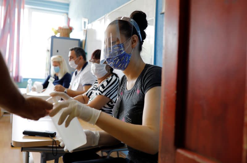 A member of an electoral commission wearing a face mask gives hand sanitiser to a voter at a polling station during the general election, in Strumica