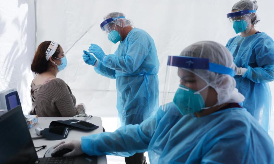 Workers prepare to test a woman for Covid at a free mobile test clinic set up outside Walker Temple AME Church in South Los Angeles in July.