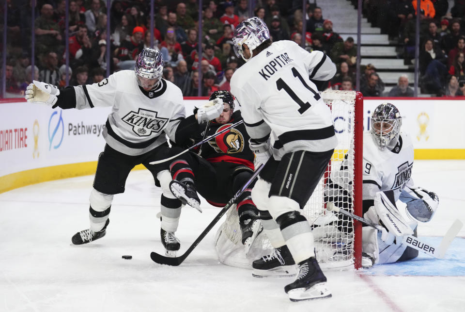 Ottawa Senators right wing Drake Batherson, second from left, gets hit to the ice by Los Angeles Kings defenseman Matt Roy, left, as Kings center Anze Kopitar (11) takes the puck during the third period of an NHL hockey game Thursday, Nov. 2, 2023, in Ottawa, Ontario. (Sean Kilpatrick/The Canadian Press via AP)