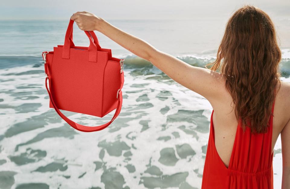 Woman on the beach holds up Rothy's new Handbag in poppy red.