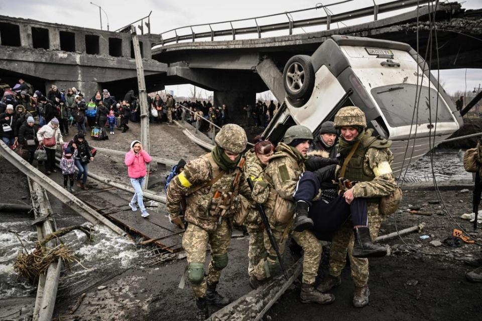Ukrainian servicemen assist people in crossing a destroyed bridge as they evacuate from Irpin, Ukraine, amid Russia's full-scale invasion of Ukraine on March 5, 2022. (Aris Messinis/AFP via Getty Images)