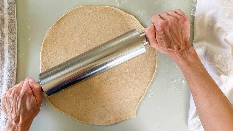 Rolling out flatbread dough on a floured surface with rolling pin