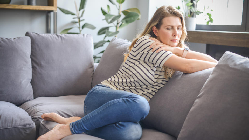 A blonde woman in a striped shirt and jeans sitting on a couch while dealing with anxiety