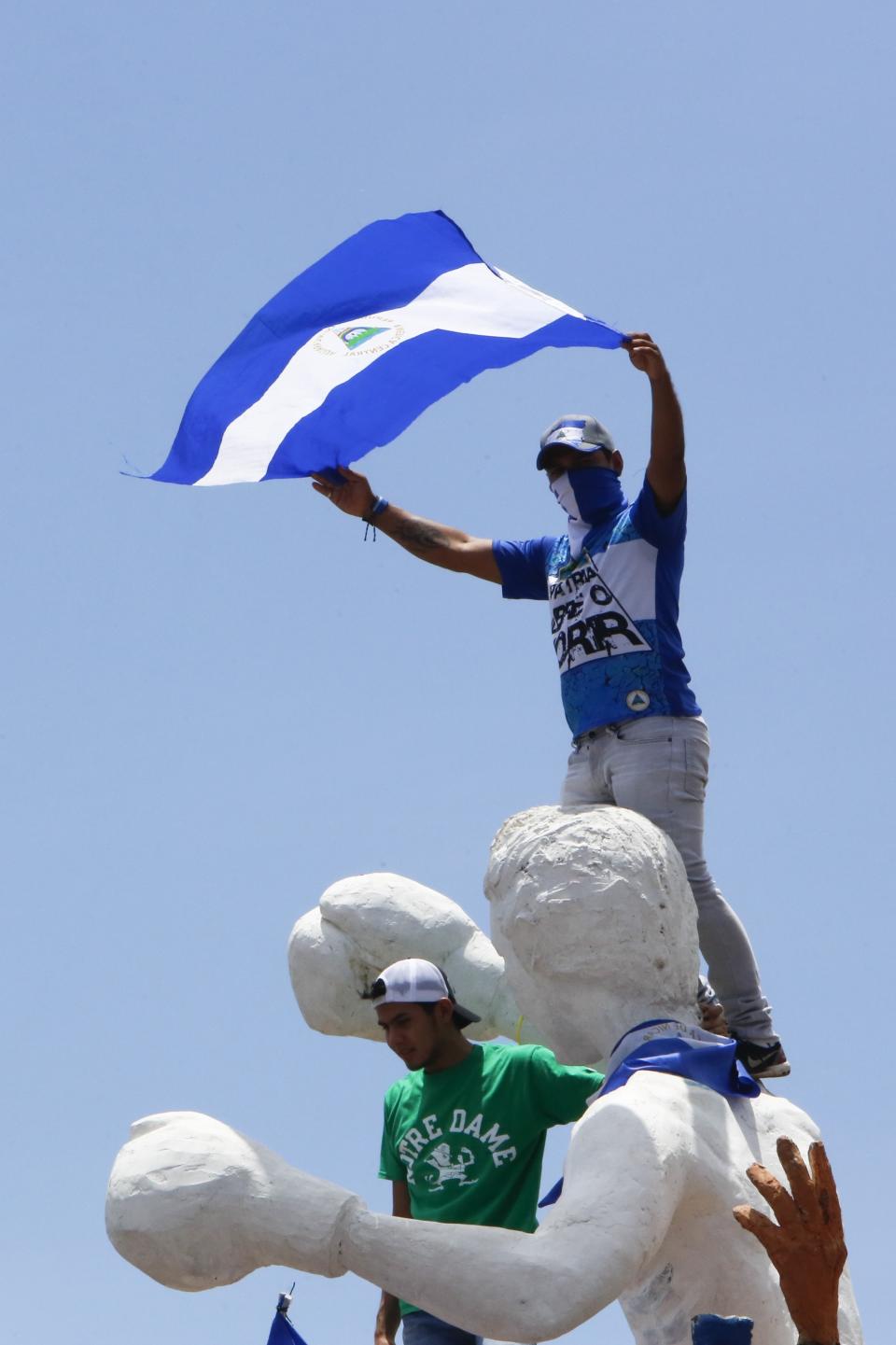 An anti-government demonstrator balances himself waving a national on a statue honoring Nicaraguan boxer Alexis Arguello demanding the resignation of President Daniel Ortega and the release of all political prisoners, during a march in support of the Catholic church, in Managua, Nicaragua, Saturday, July 28, 2018. At least 448 people have been killed, most of them protesters, since the protests began in April. Demonstrators were initially upset over proposed social security cuts but are now demanding Ortega leave office after a deadly crackdown by security forces and armed pro-government civilians. (AP Photo/Alfredo Zuniga)