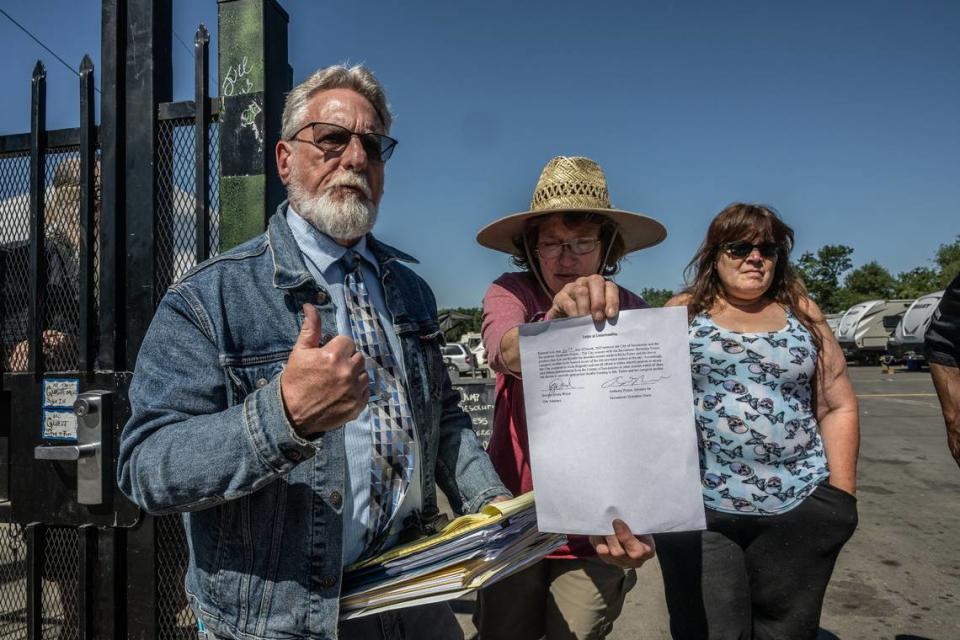 Sharon Jones, center, a leader of Camp Resolution, holds up an agreement between city of Sacramento’s attorney and Sacramento Homeless Union lawyer Anthony Price, left, to “work diligently and use all efforts” to find housing for Holly Porter and her live-in caregiver mother, at a press conference at the self- governing Sacramento homeless encampment Tuesday.