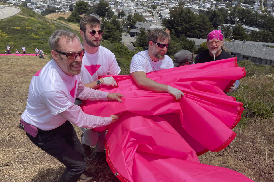 Patrick Carney, left, Co-Founder of Friends of the Pink Triangle, works with volunteers laying out pink tarps to form the shape of a pink triangle on Twin Peaks in San Francisco, Friday, June 16, 2023. Hundreds of volunteers installed the giant pink triangle made out of cloth and canvas and with pink lights around its edges last week as part of the city's Pride celebrations. It's an annual tradition that started in 1995 but this year's triangle is nearly an acre in size and can be seen up to 20 miles (32 kms.) away. (AP Photo/Haven Daley)