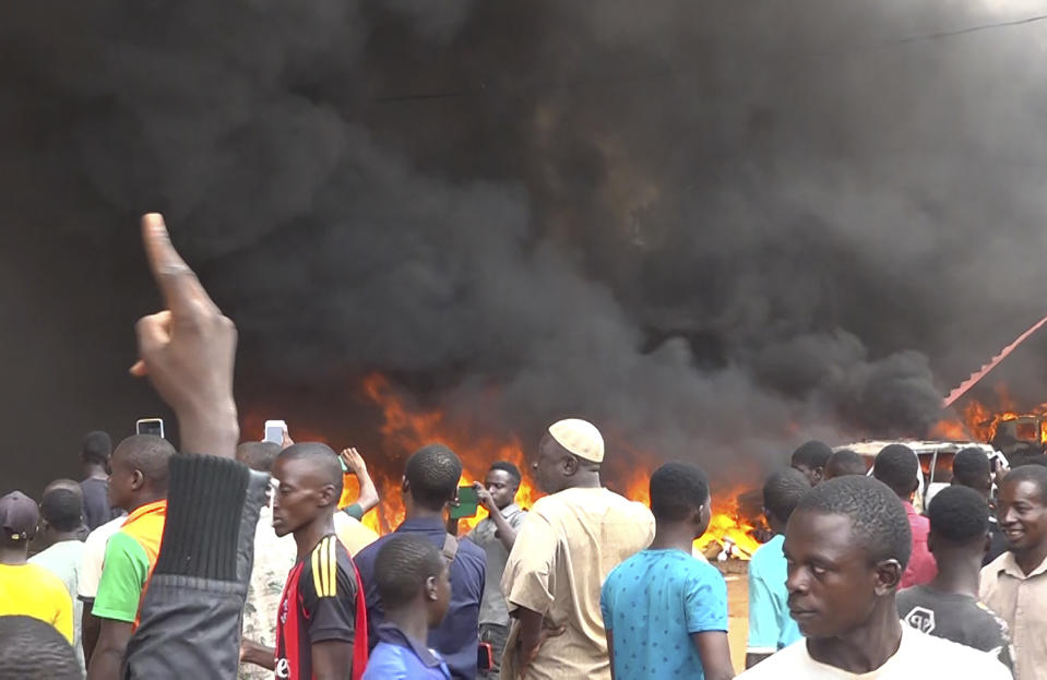 With the headquarters of the ruling party burning in the back, supporters of mutinous soldiers demonstrate in Niamey, Niger, Thursday, July 27 2023. Governing bodies in Africa condemned what they characterized as a coup attempt Wednesday against Niger's President Mohamed Bazoum, after members of the presidential guard declared they had seized power in a coup over the West African country's deteriorating security situation. (AP Photo/Fatahoulaye Hassane Midou)