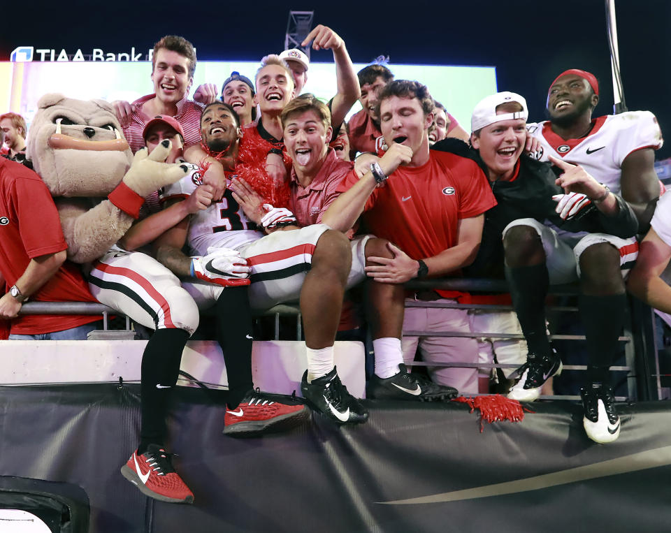 Georgia tailback Brian Herrien, center left, climbs into the stands to celebrate the team's 24-17 victory over Florida with the fans, mascot Hairy Dawg, left, and defensive back Richard LeCounte, right, after an NCAA college football game Saturday, Nov. 2, 2019, in Jacksonville, Fla. (Curtis Compton/Atlanta Journal Constitution via AP)