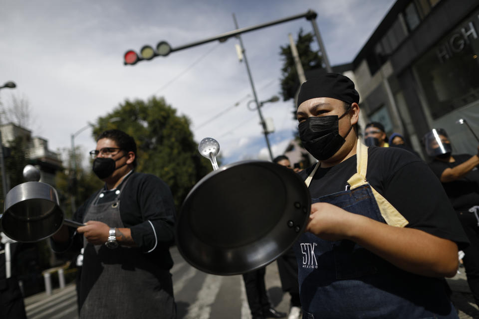 Restaurant workers bang metal pots as more than a hundred employees from multiple restaurants blocked a street in the Polanco neighborhood to protest against COVID-19 "red alert" restrictions that have closed on-site dining, in Mexico City, Tuesday, Jan. 12, 2021. More than three weeks into Mexico City's second pandemic shutdown, restaurateurs desperate to save their businesses and maintain their employees are uniting under the slogan "Open or Die" ("Abrir o morir" in Spanish), to pressure the city government to allow them to operate with limited seating and protective health measures. (AP Photo/Rebecca Blackwell)