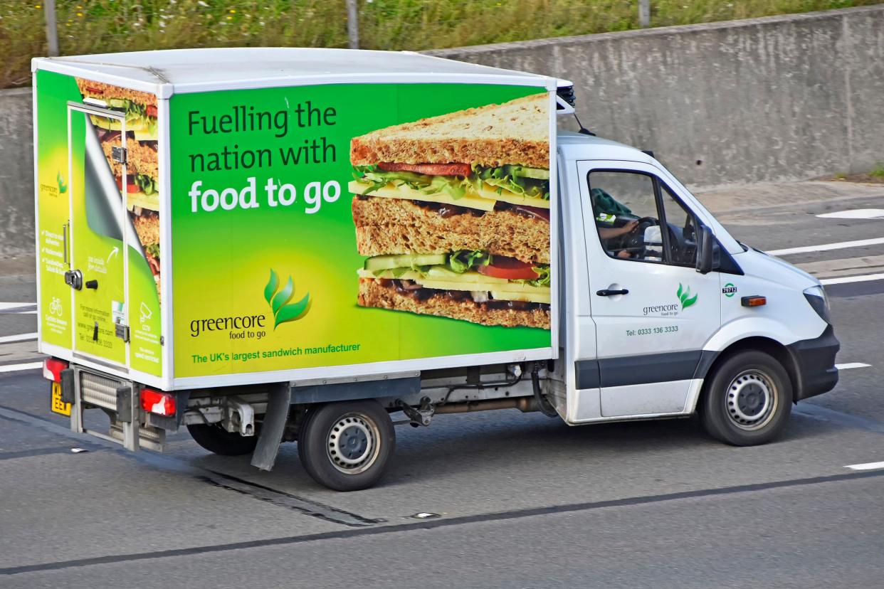 Side & back view graphics on Greencore sandwich manufacturing business 'food to go' supply chain delivery van & driver on motorway in Essex England UK