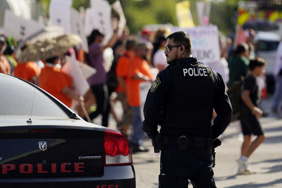 A Uvalde police officer watches as family and friends of those killed and injured in the school shootings at Robb Elementary take part in a protest march and rally, Sunday, July 10, 2022, in Uvalde, Texas. Families and residents are seeking answers and changes after the tragedy. (AP Photo/Eric Gay)