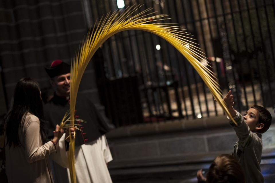 EDS NOTE : SPANISH LAW REQUIRES THAT THE FACES OF MINORS ARE MASKED IN PUBLICATIONS WITHIN SPAIN. A priest holds a palm branch while a young boy tries to catch it, right, during Palm Sunday, prior to Holy Week, in Pamplona, northern Spain, Sunday April 13, 2014. Spain's devoted Catholics take part in a lot of religious ceremonies during Holy Week. (AP Photo/Alvaro Barrientos)