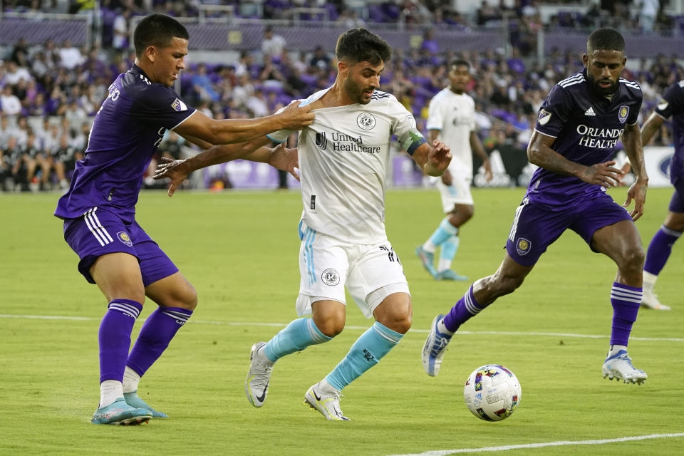 Orlando City's Cesar Araujo, left, grabs New England Revolution's Carles Gil, center, as he tries to stop him from advancing the ball as teammate Ruan, right, comes in to assist during the first half of an MLS soccer match, Saturday, Aug. 6, 2022, in Orlando, Fla. (AP Photo/John Raoux)