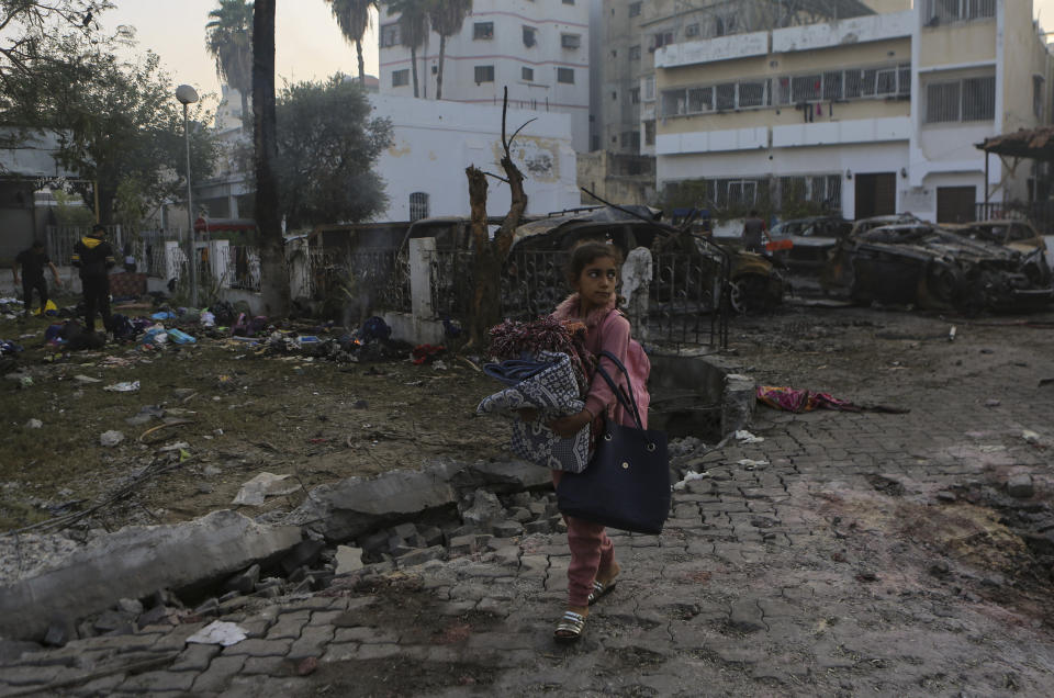 A Palestinian girl carries a blankets as she walks past the explosion science at al-Ahli hospital, in Gaza City, Wednesday, Oct. 18, 2023. The Hamas-run Health Ministry says an Israeli airstrike caused the explosion that killed hundreds at al-Ahli, but the Israeli military says it was a misfired Palestinian rocket. (AP Photo/Abed Khaled)