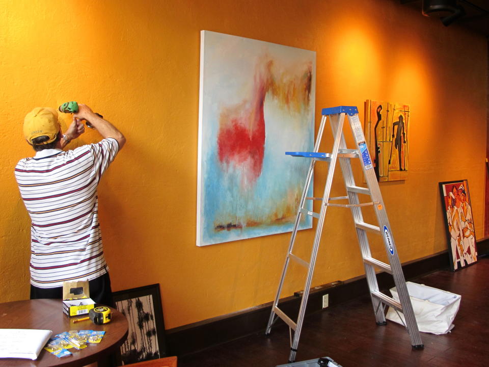 A worker hangs paintings at Table 118, a new restaurant in Lake City, S.C., as part of the ArtFields arts festival on Thursday, April 18, 2013. The 10-day arts festival runs from April 19 through April 28, 2013. Many of the 400 works of art are being displayed in businesses in this old tobacco town. (AP Photo/Bruce Smith)