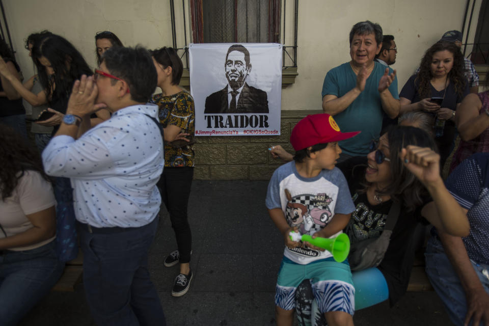 Demonstrators protest against Guatemalan President Jimmy Morales, featured in the poster that reads in Spanish "Traitor," outside the Presidential House in Guatemala City, Saturday, July 27, 2019. Demonstrators are protesting an agreement that the president signed with Washington to require migrants passing through the Central American country to seek asylum there, rather than pushing on to the U.S. (AP Photo/ Oliver de Ros)