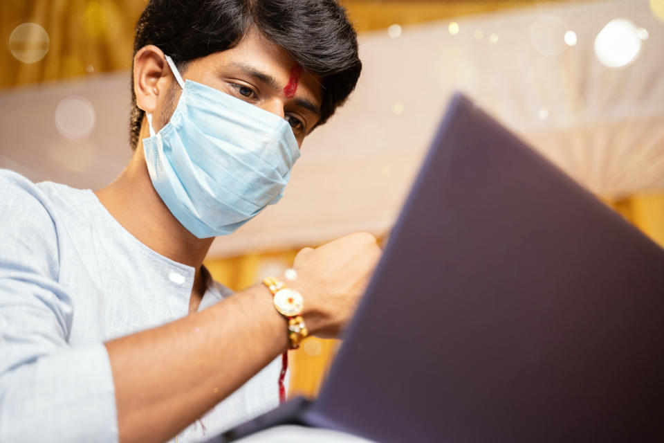 young man with medical mask making video call and showing Rakhi or Raksha Bandhan to his sister or family friends after festival ceremony during coronavirus ot covid-19 pandemic