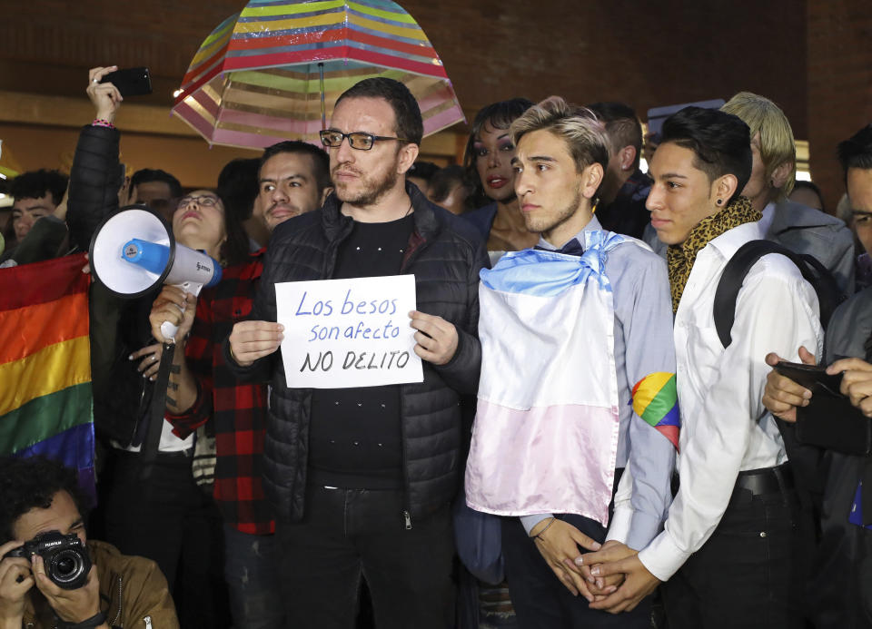 Esteban Carrillo, 24, second from right, holds hands with Nicolas Tellez, 19, during a "kiss-a-thon," a form of protest for LGBT rights in Bogota, Colombia, Wednesday, April 17, 2019. The event was held at the same Andino shopping mall where days ago the two were harassed by a customer who lured police into fining them for "exhibitionism." The sign reads in Spanish "Kisses are affection, not a crime." (AP Photo/Fernando Vergara)