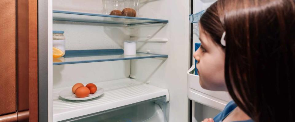 Worried girl looking at the almost empty fridge due to a crisis